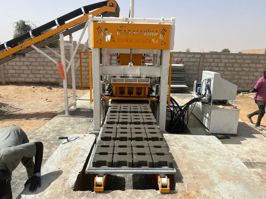 BLOCKMASTER 4 block machine front view with belt conveyor, control panel and loaded pallets on the roller table, Senegal