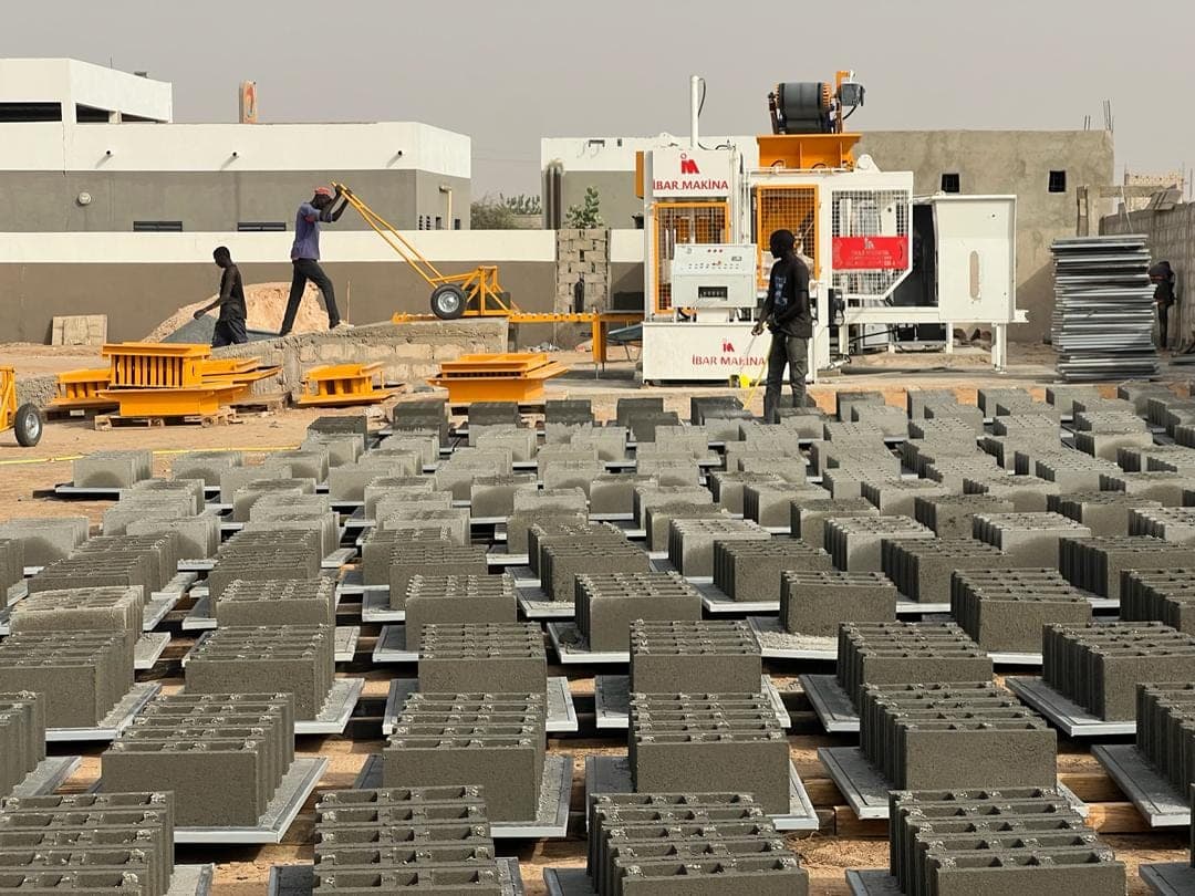 Workers moving pallets with a pallet trolley across the curing yard of the BLOCKMASTER 4 plant, Senegal