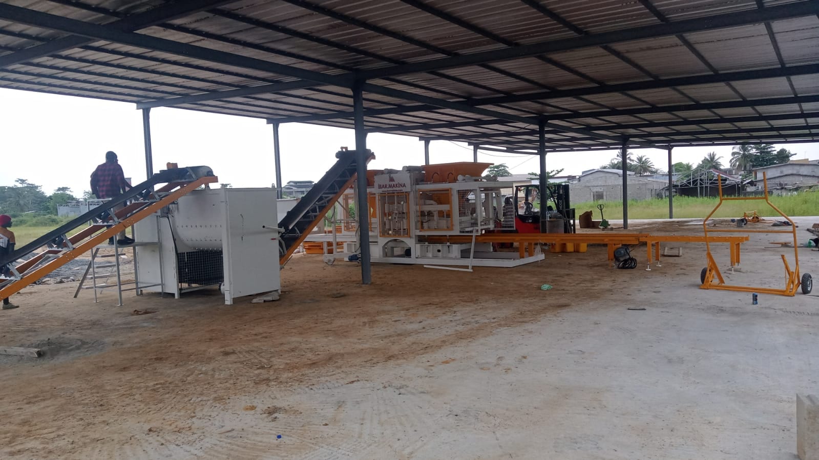 Usine de parpaings au Gabon : malaxeur, convoyeurs à bande inclinés et machine CBM 25 sous un hangar métallique